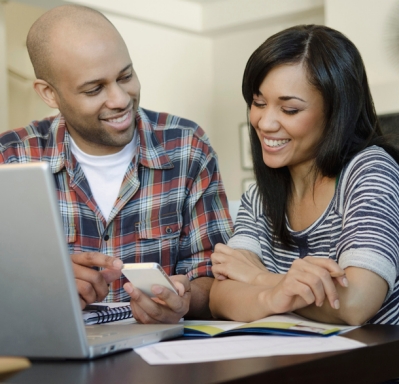 Young couple looking at phone with laptop nearby